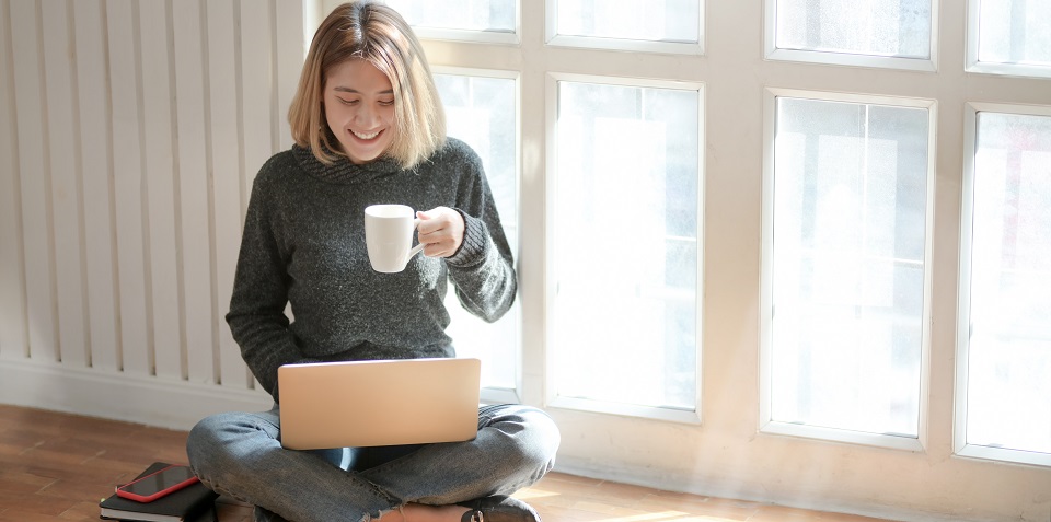 Woman sitting down drinking coffee whilst on laptop